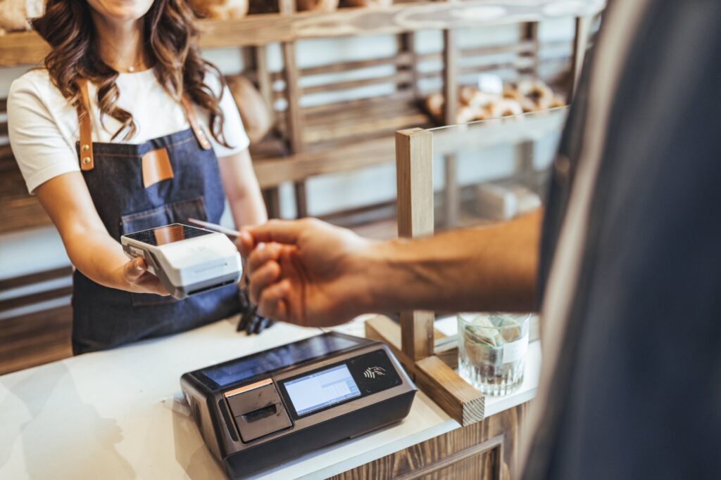 A merchant accepts a contactless card payment at a bakery counter